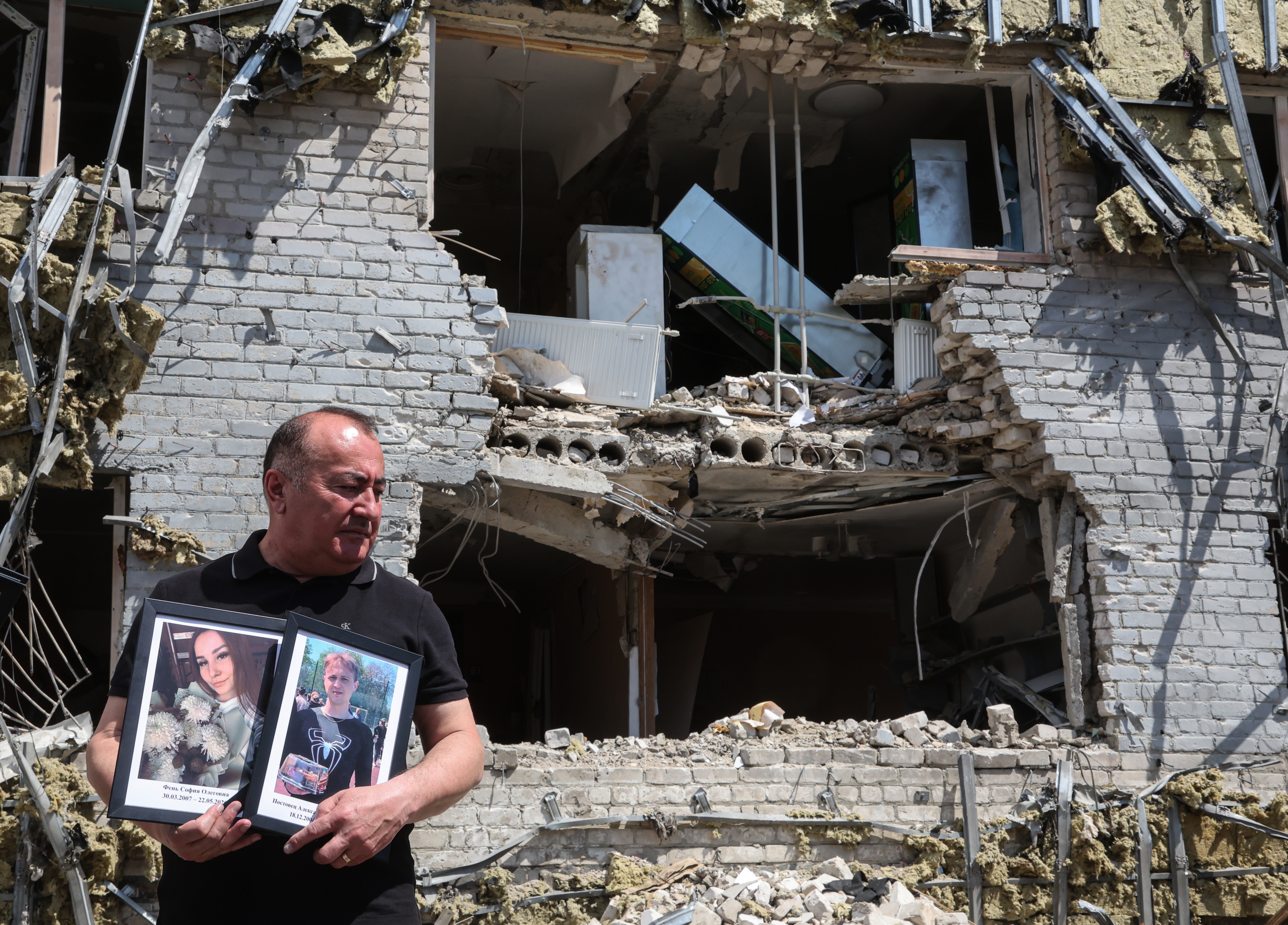 Un profesor de la Universidad Pedagógica Estatal de Luhansk sosteniendo retratos de los estudiantes fallecidos, frente a un edificio de residencia universitaria dañado por drones ucranianos en Starobilsk. Foto: EFE | EPA | Sergei Ilnitsky.