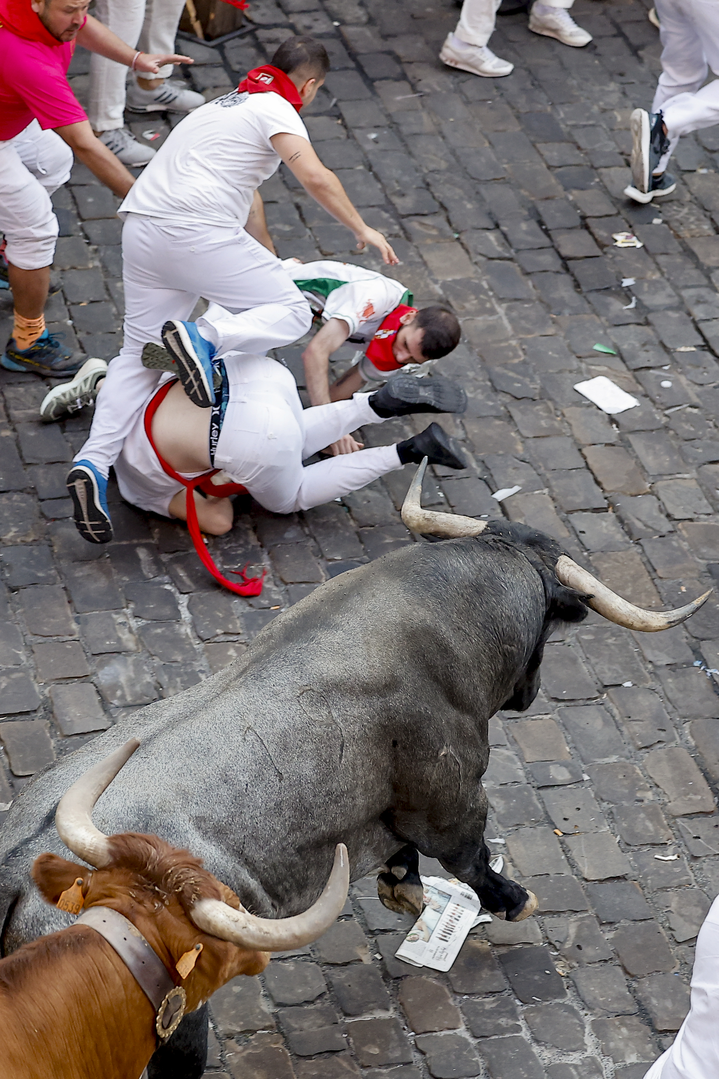 Un mozo tropieza sobre otros compañeros caídos al paso de los toros de la ganadería de José Escolar Gil por la Plaza Consistorial entrada a Mercaderes durante el quinto encierro de los Sanfermines 2026 en Pamplona. Foto: EFE | Villar López.