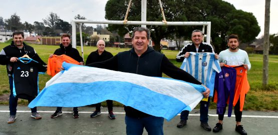 Alberto Martínez, papá de "Dibu", sostiene la bandera argentina. Detrás, ex compañeros y formadores con las camisetas del arquero marplatense.