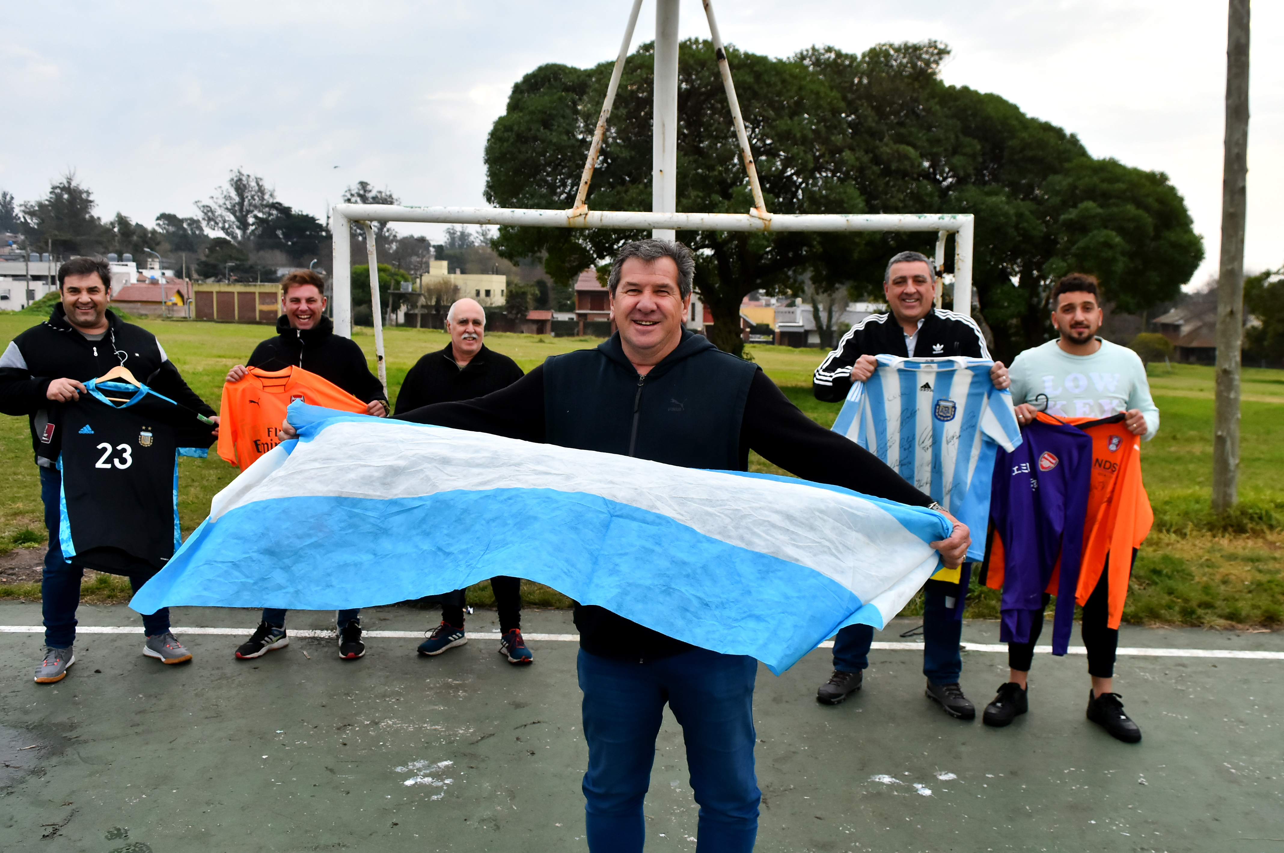 Alberto Martínez, papá de "Dibu", sostiene la bandera argentina. Detrás, ex compañeros y formadores con las camisetas del arquero marplatense. 