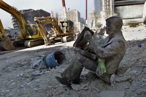 A dust covered bronze statue of a man with his briefcase rests in the rubble of the World Trade Center towers September 13, 2001 in New York. The statue once rested on a bench near the towers and now holds flowers and a note reading " In memory of all who gave their lives and try to save so many". REUTERS/POOL/Beth A. Keiser