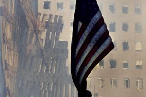 A flag hangs at half staff with the remains of the World Trade Center disaster in the background in New York September 17, 2001. The twin towers of the World Trade Center collapsed after being struck by two hijacked jetliners on September 11.  REUTERS/Mike Segar