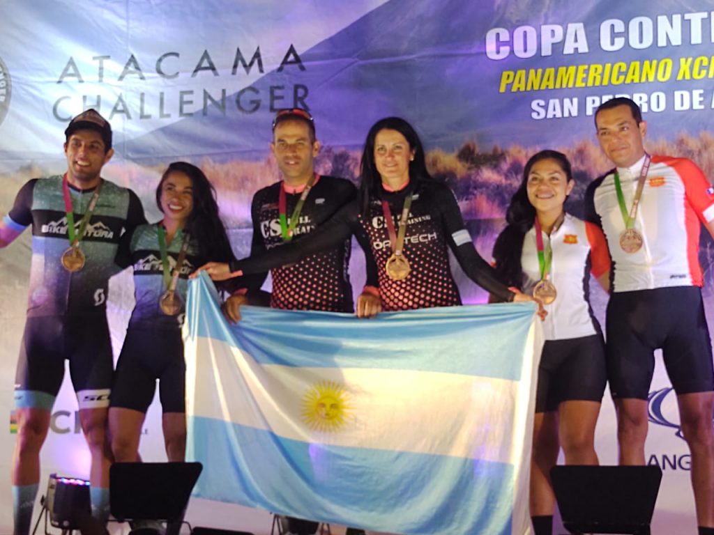 Sergio Ramos y Corina Butti posan con medallas y bandera argentina en el centro del podio.