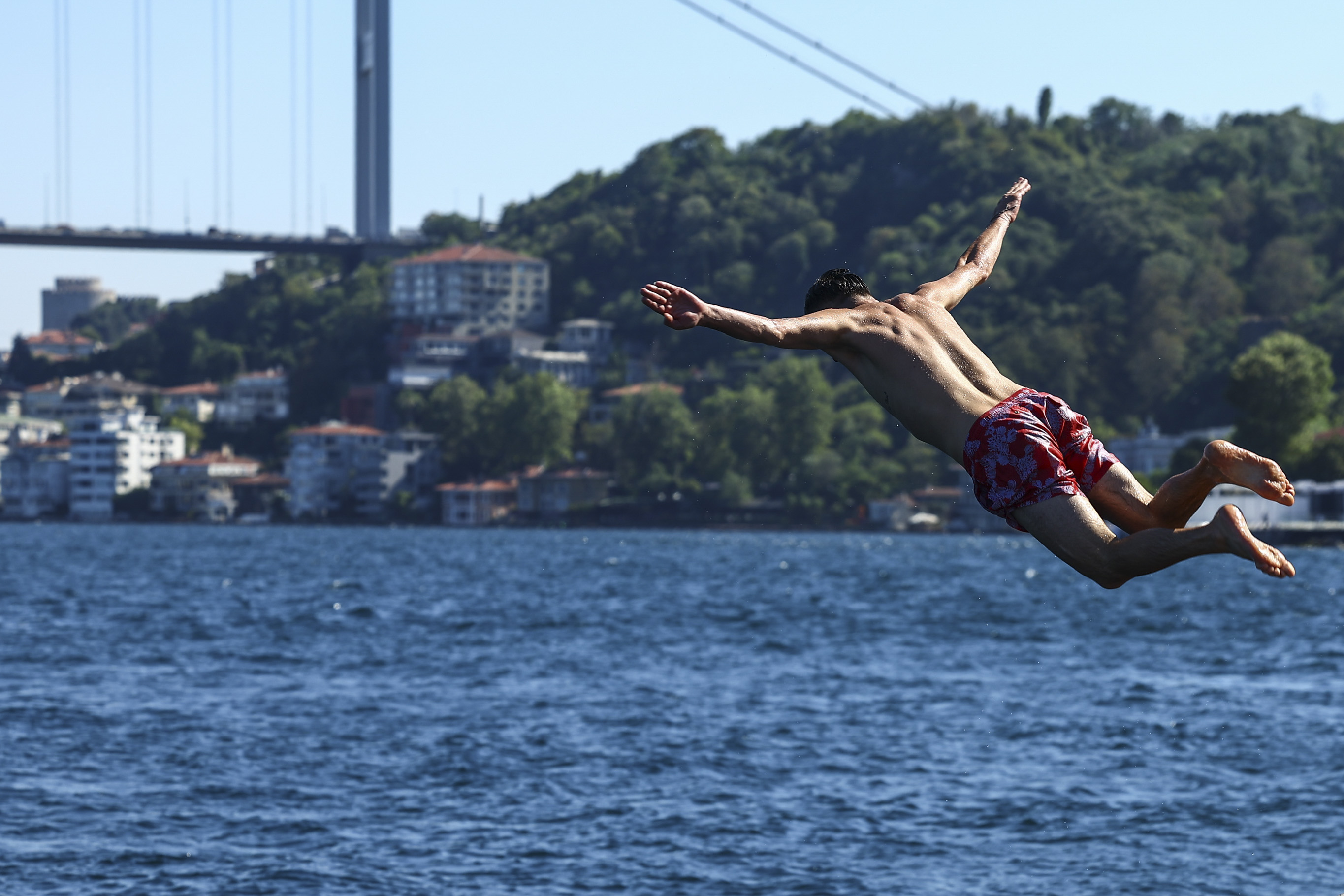 Un hombre salta al Bósforo frente al puente Fatih Sultan Mehmet en un día muy caluroso de verano en Estambul, Turquía. Foto: EFE | EPA | Sedat Suna.