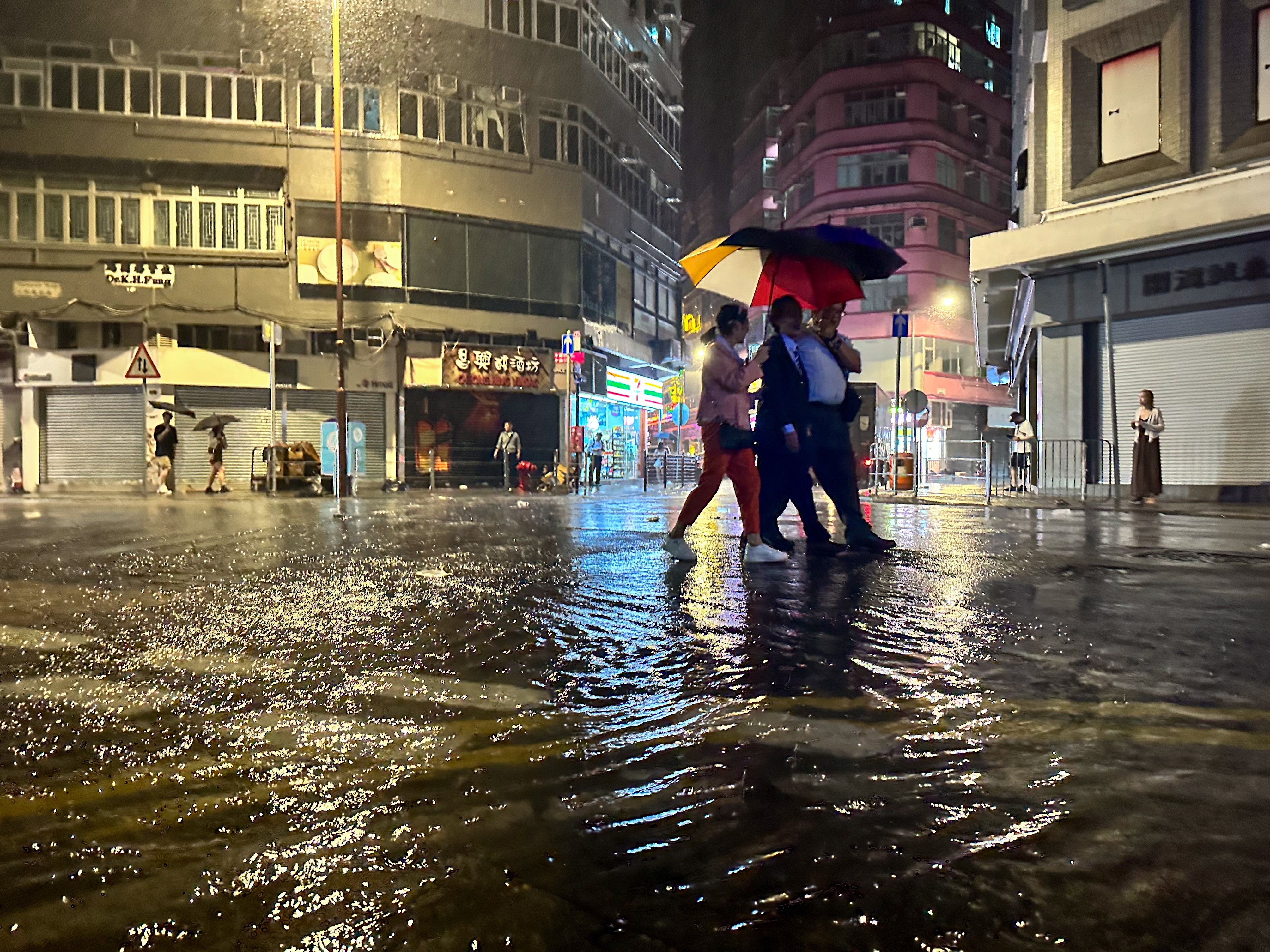 Varias personas comparten un paraguas en una calle inundada, mientras continúan las lluvias torrenciales después del paso del tifón en Hong Kong. Foto: EFE | Daniel Ceng.