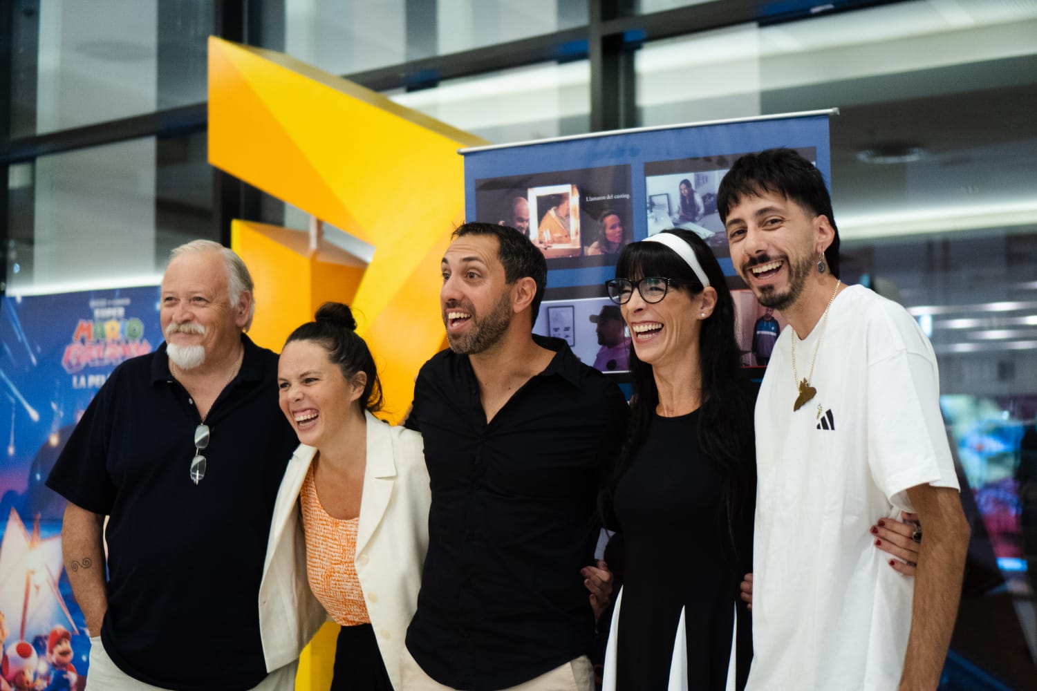 Los actores y las actrices de la película, en el hall del Paseo Aldrey, con el afiche de la película detrás.